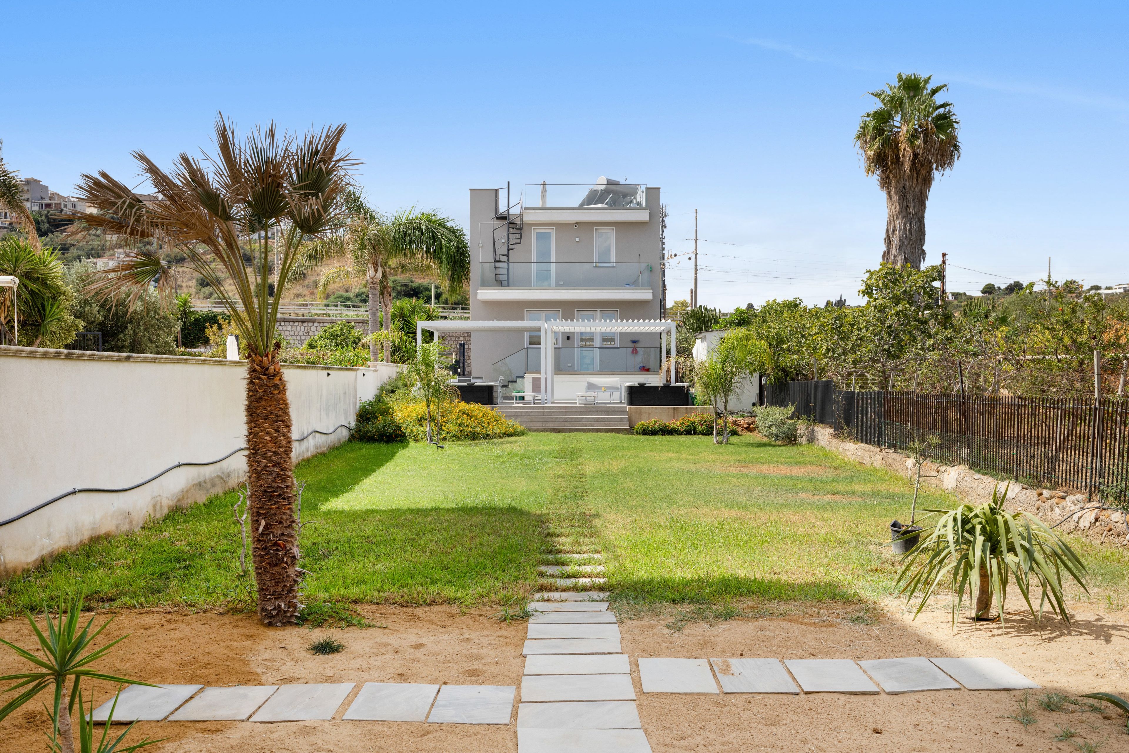 A modern two-story house with a visible staircase leading to the upper floor, surrounded by a well-maintained lawn and various plants.