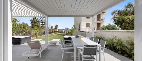 Eine Außenpatio mit einer weißen Pergola, einem langen Esstisch mit Stühlen und Blick auf den Garten.