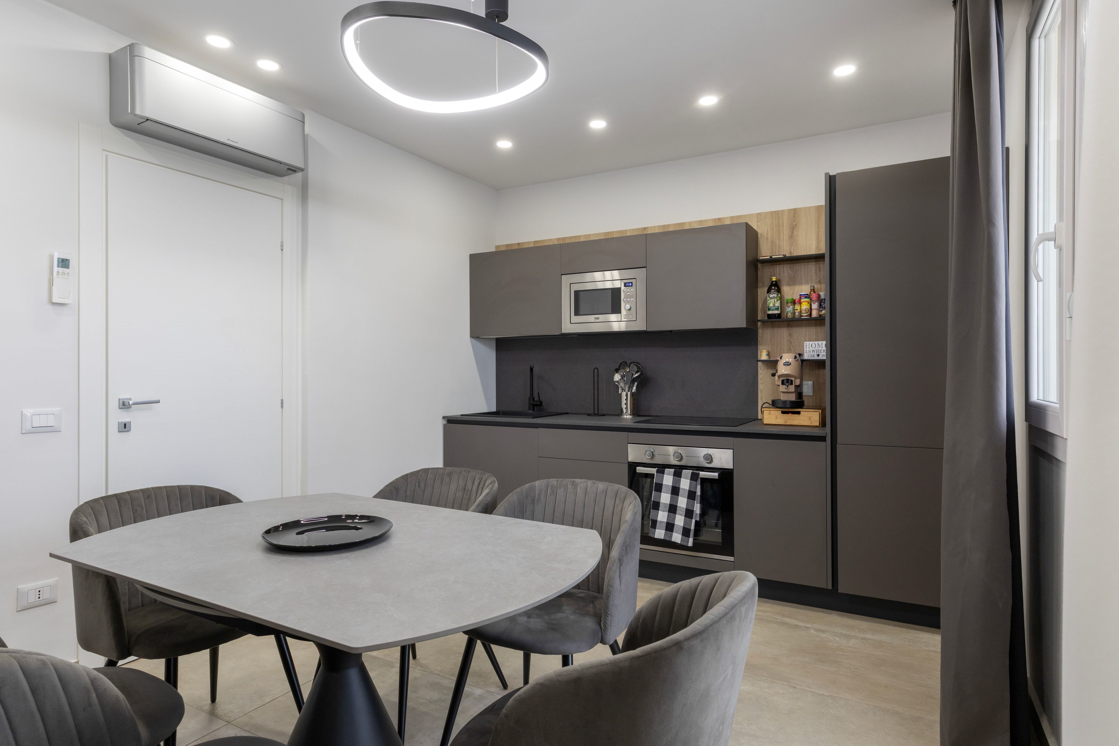 A modern kitchen with built-in appliances, a dining area with a table and chairs, and a window with curtains.