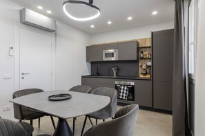 A modern kitchen with built-in appliances, a dining area with a table and chairs, and a window with curtains. - Villa 'Zefira Mare' with Sea View, Wi-Fi, and Air Conditioning (Altavilla Milicia)