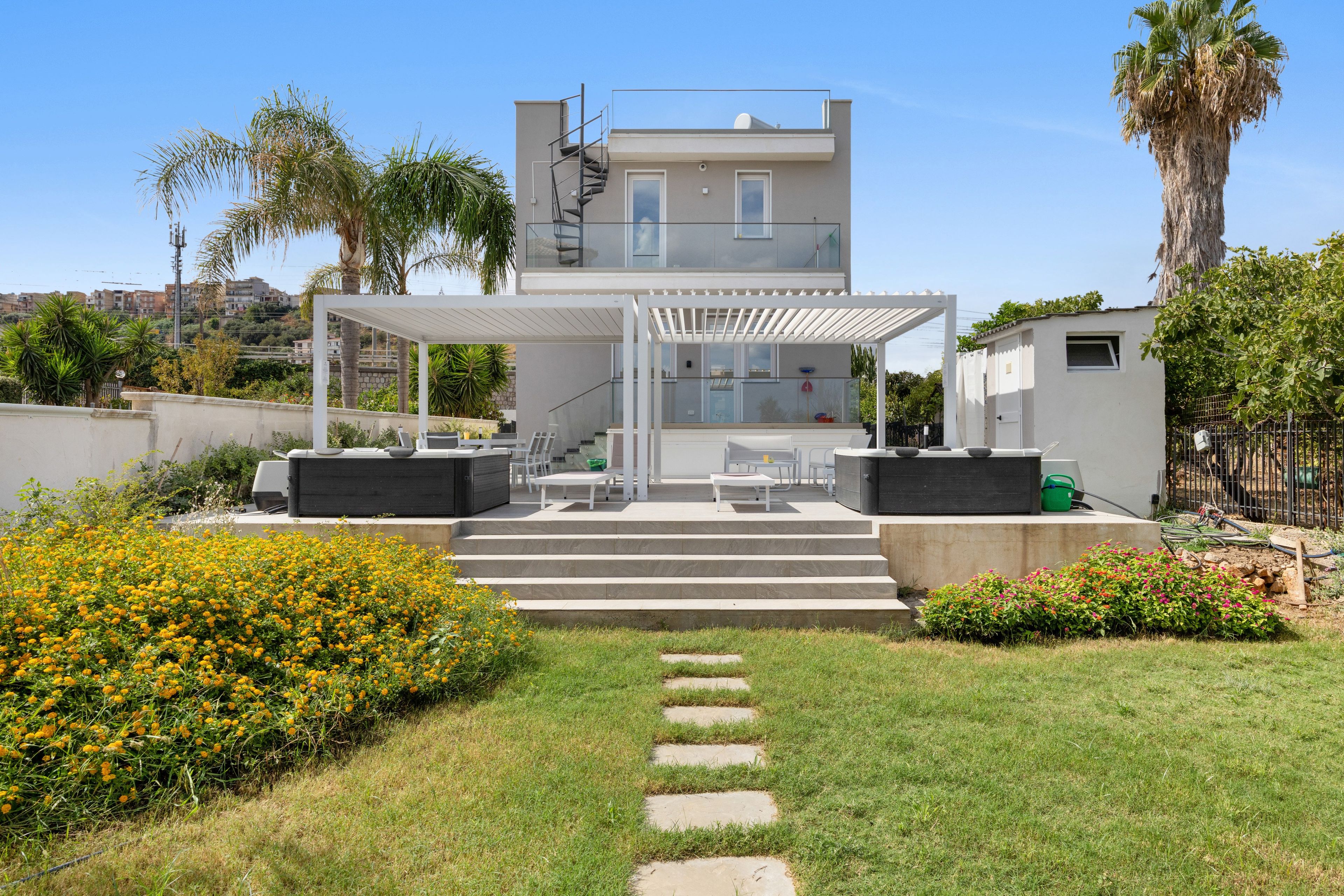 A modern two-story house with a covered patio, outdoor seating, and a well-maintained garden.