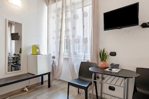 Una camera moderna con TV a schermo piatto, un piccolo frigorifero, un tavolo da pranzo con sedie, uno specchio e una pianta in vaso.