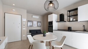 Une cuisine moderne avec des meubles blancs, une table de salle à manger ronde entourée de chaises, un luminaire suspendu noir et une petite plante en pot.