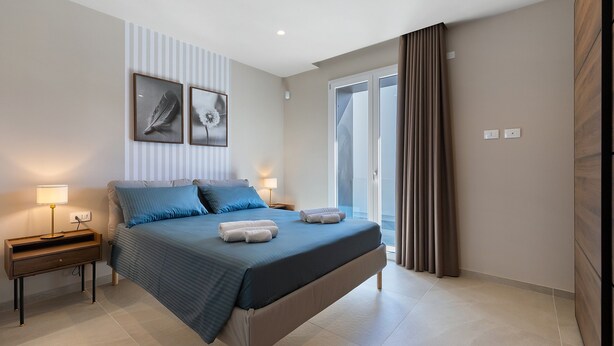 Une chambre à coucher comprenant un lit, des tables de chevet, une lampe, un tableau accroché au mur et une porte-fenêtre coulissante.