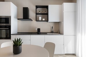 Une cuisine moderne avec des armoires blanches, un comptoir noir, un four à micro-ondes encastré, une machine à café et une plante en pot posée sur la table.