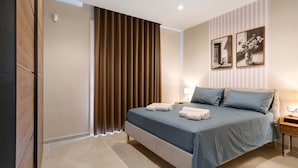 Un dormitorio con cama, cortinas, una mesita de noche y dos cuadros colgados en la pared.