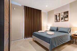 Un dormitorio con cama, cortinas, una mesita de noche y dos cuadros colgados en la pared.