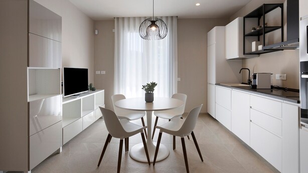 Una cocina moderna con armarios blancos, una mesa de comedor con sillas, una lámpara colgante y un televisor de pantalla plana.