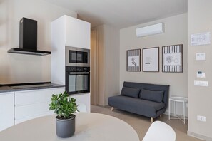 Une cuisine moderne dotée d’appareils électroménagers intégrés, un canapé gris et une petite table sur laquelle est posée une plante en pot.