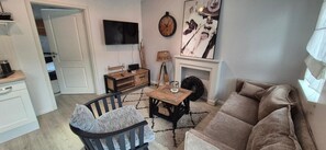 Una sala de estar con sofá, sillón, mesa de centro, televisor, chimenea y un reloj en la pared.