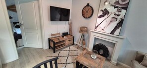 Una habitación con televisión, chimenea, un mueble de madera, lámpara y un cuadro.