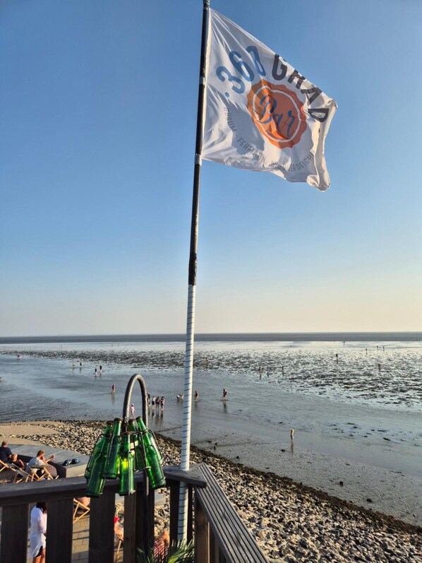 Escena de playa con una bandera, una terraza de madera y cielo despejado.