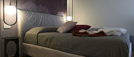A modern bedroom with a large bed, two pendant lights, a small side table, and a textured wall.