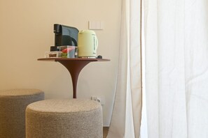 A small table with a coffee maker, a kettle, and a box of tissues. There are two ottomans and a curtain. - COBALTO Room- Aurisea Luxury Stays (Bari)