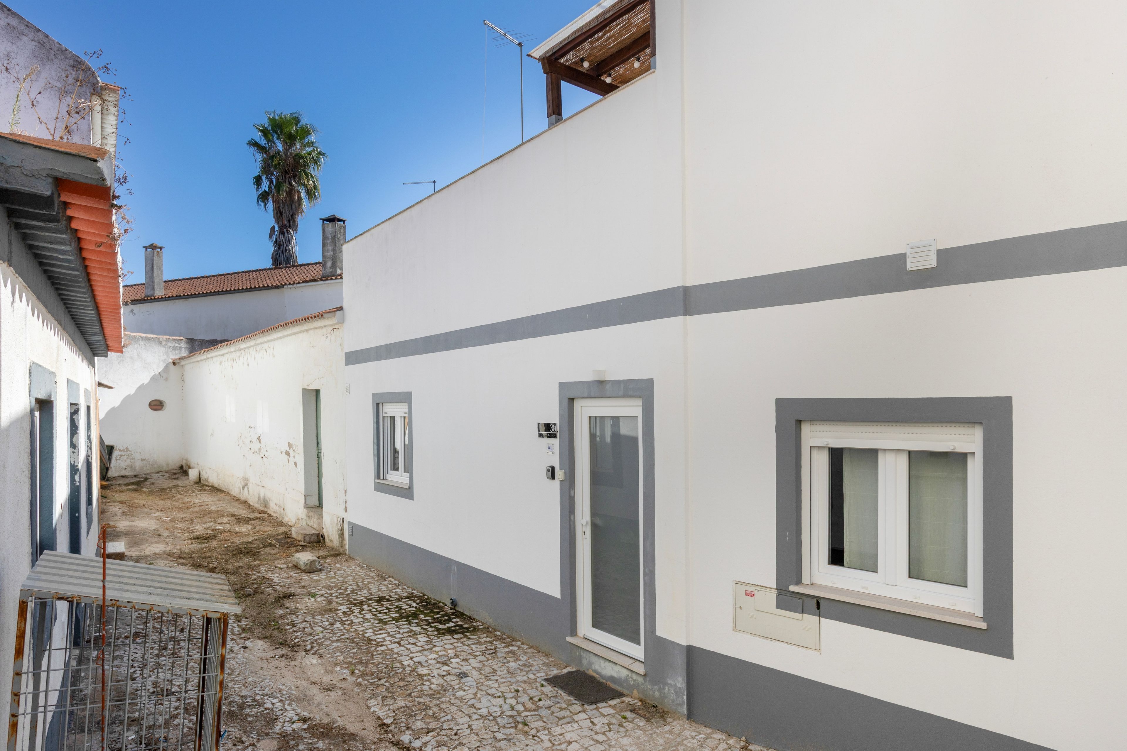 Une ruelle étroite avec un bâtiment blanc orné d’une bande grise, une porte et une fenêtre.