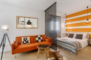 Quarto de hotel moderno com sofá, cama, espelho grande e parede listrada.