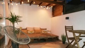 Una zona relax all'aperto accogliente, con una panca imbottita, un poggiapiedi in vimini e un tavolo da pranzo con sedie.