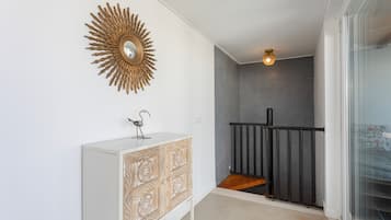 A hallway with a white cabinet, a decorative sunburst mirror, a small metal sculpture, and a staircase with a black railing.