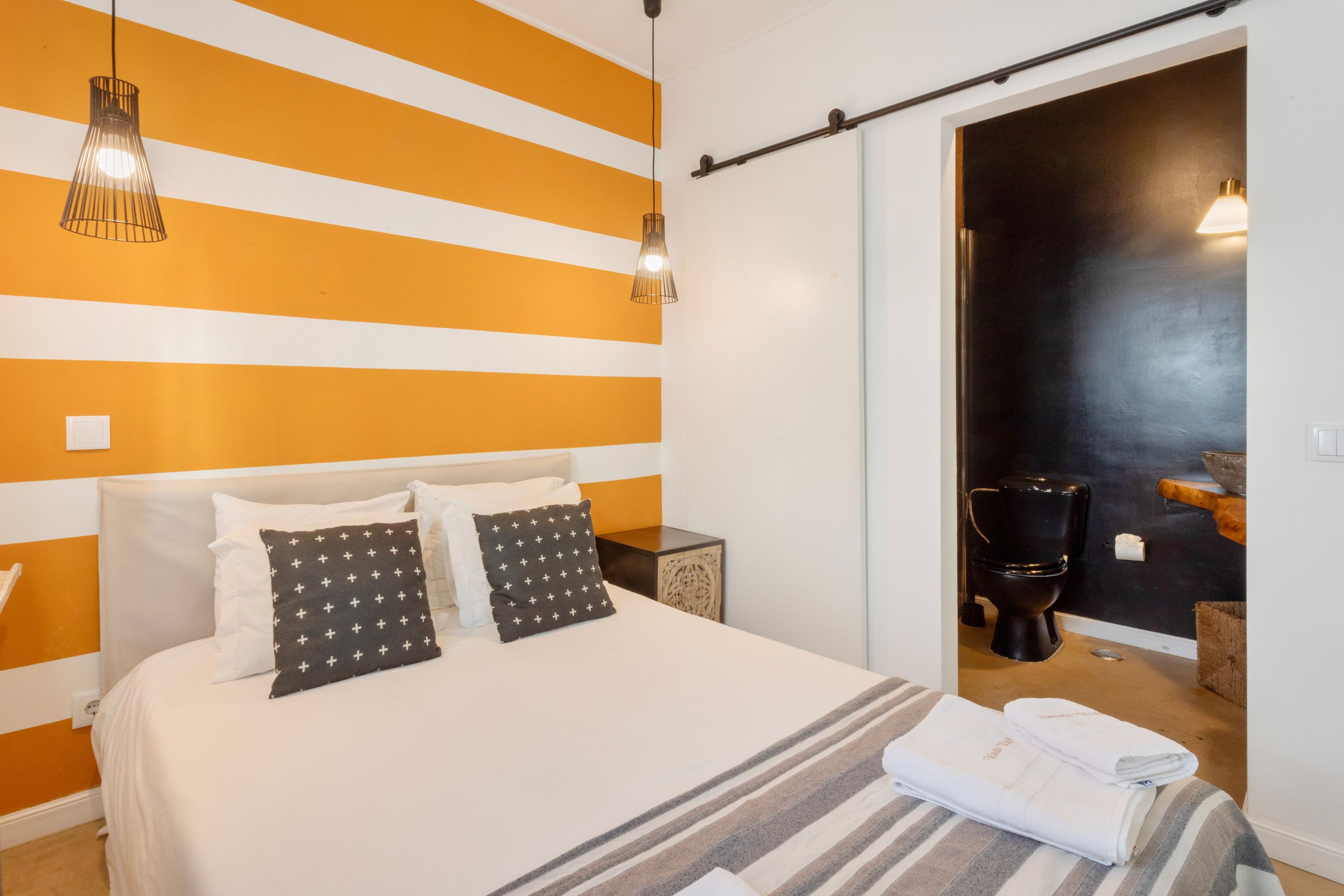Ein Hotelzimmer mit Bett, zwei Nachttischlampen, einem Nachttisch und einem durch eine offene Tür einsehbaren Badezimmer.