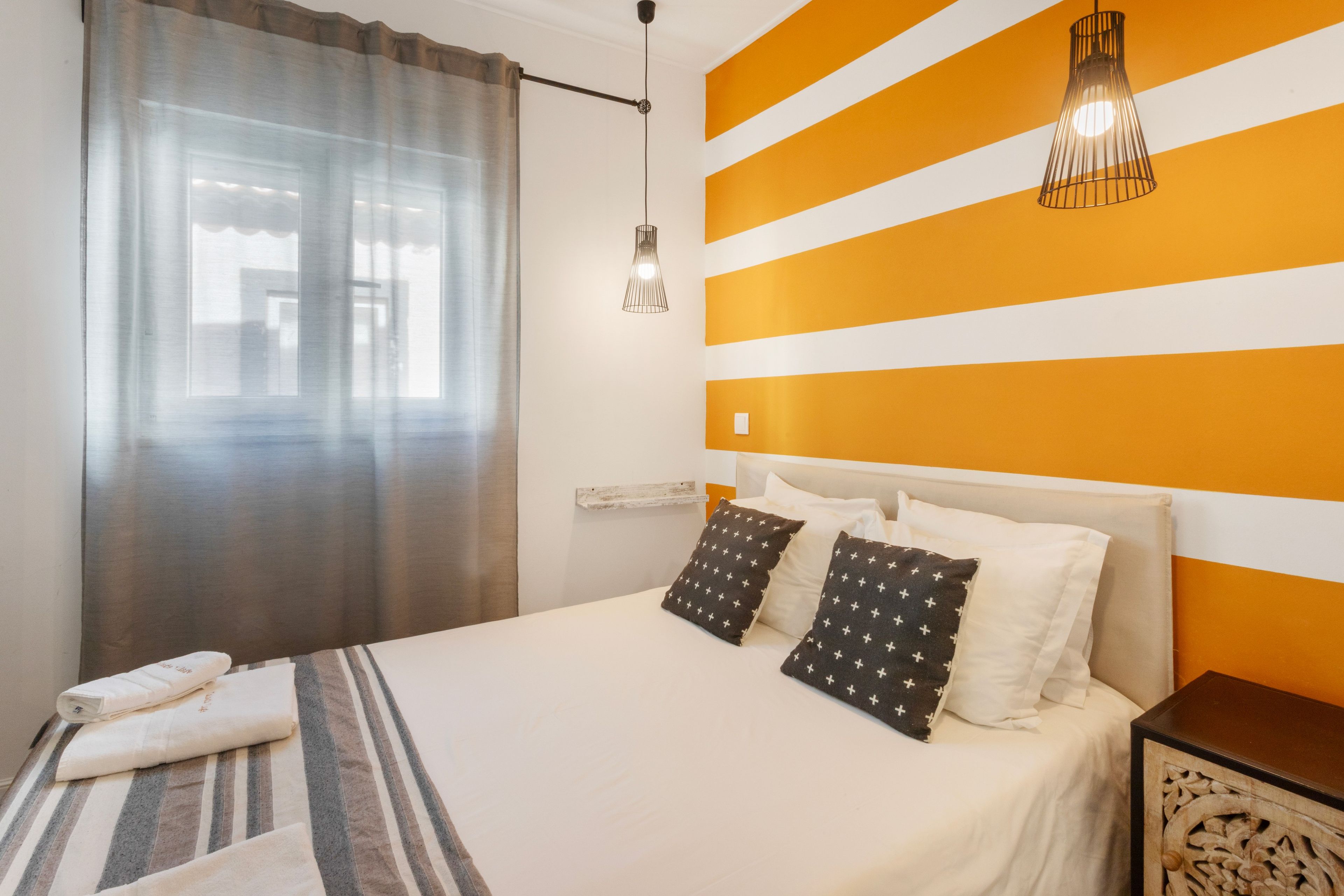 A hotel room with a bed, a nightstand, a lamp, and a window with curtains.