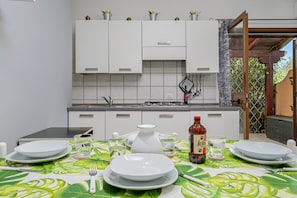 A kitchen with white cabinets, a dining table set with plates, glasses, and cutlery, and a bottle of sauce on the table.