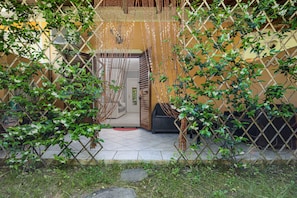 Zona d'estar a l'aire lliure coberta, amb una tanca de reixeta, un sofà de vimet i una porta que dona a l'interior.