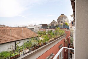 Ein Balkon mit Blumentöpfen, ein rotes Gebäude und eine kuppelartige Struktur im Hintergrund.