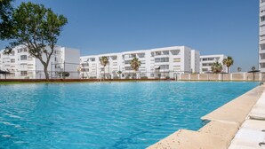 Une piscine à l’eau d’un bleu cristallin, entourée de bâtiments blancs dotés de balcons et de palmiers.