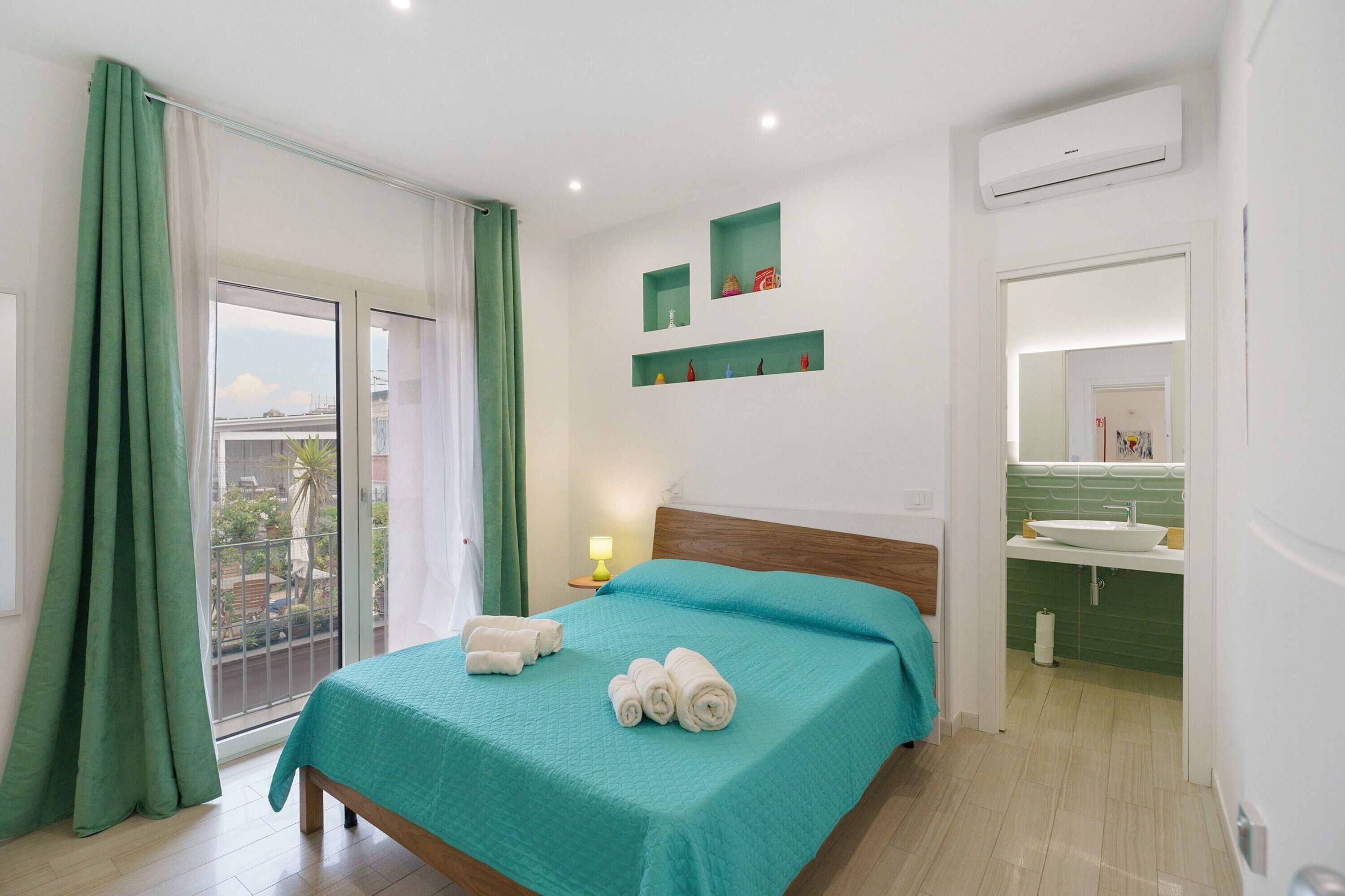 A hotel room with a bed, a bathroom, a balcony, and a view of the outside.