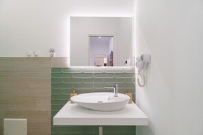 Un baño con lavamanos blanco, espejo, secador de pelo y toallero.