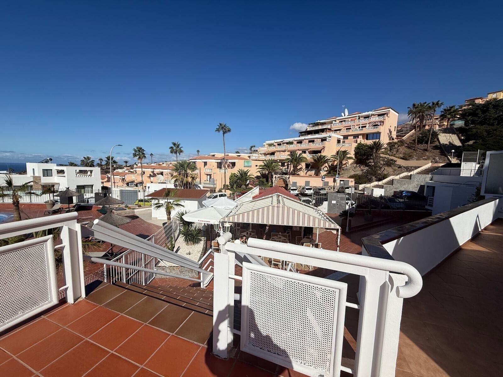 A rooftop terrace with a view of a coastal town, including buildings and palm trees.