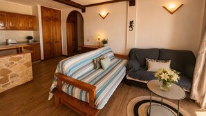 A cozy room with a bed, a sofa, a small table with a vase of flowers, wooden beams on the ceiling, and a kitchen area in the background. - Vacation Apartment 'Maika's' with Sea View, Shared Pool and Wi-Fi (Costa Adeje)
