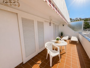 Un balcon avec des volets blancs, une petite table sur laquelle est posée une plante en pot, des chaises en plastique blanches et un parasol blanc.