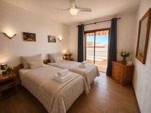 Une chambre d’hôtel avec deux lits, un ventilateur de plafond, un balcon avec vue et une commode en bois.