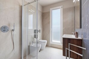 Un baño moderno con cabina de ducha de vidrio, un bidé, un inodoro y un tocador de madera con espejo.