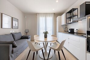 A modern kitchen with white cabinets, a dining area with a round table and chairs, and a grey sofa with cushions. - Apartment 'Bora' with Balcony, Wi-Fi and Air Conditioning (Santa Flavia)