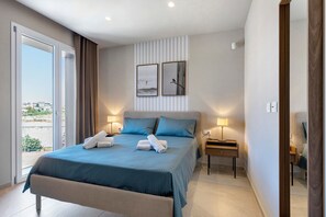 Une chambre d’hôtel avec un grand lit, deux tables de chevet avec des lampes, une vue à travers une porte coulissante et un tableau accroché au mur.