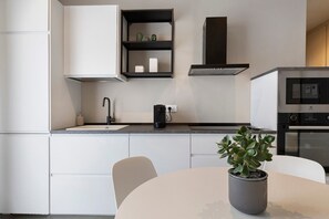 A modern kitchen with white cabinets, a black countertop, a coffee machine, a potted plant, and a built-in oven. - 'Bora' Apartment with Balcony, Wi-Fi and Air Conditioning (Santa Flavia)