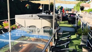 Un patio al aire libre con una mesa de vidrio, sillas de mimbre negro y plantas en macetas.