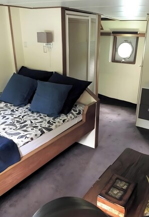 A bed with a headboard, a bedside table, a wall-mounted light, and a window with a mirror.