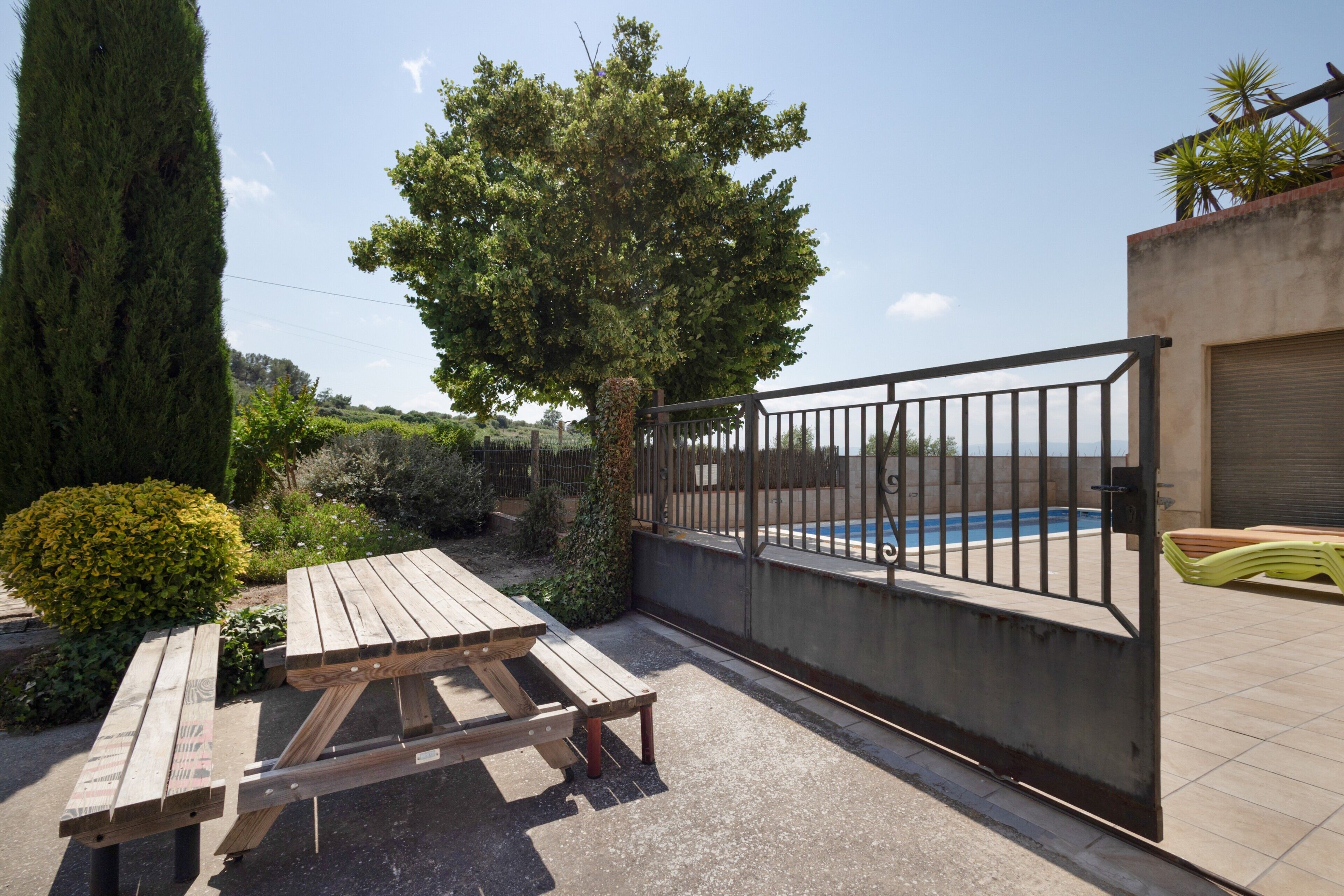 Un patio con tavolo e panche in legno, una piscina e un cancello in metallo.