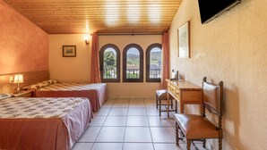 Ein Hotelzimmer mit zwei Betten, einem Schreibtisch, einem Sessel, einem an der Wand befestigten Fernseher und einem Fenster mit Blick ins Freie.