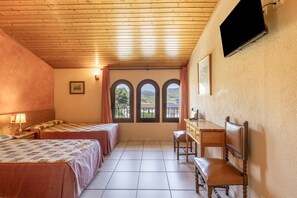 Habitación de hotel con dos camas, un escritorio, una silla, un televisor fijado a la pared y una ventana con vistas al exterior.