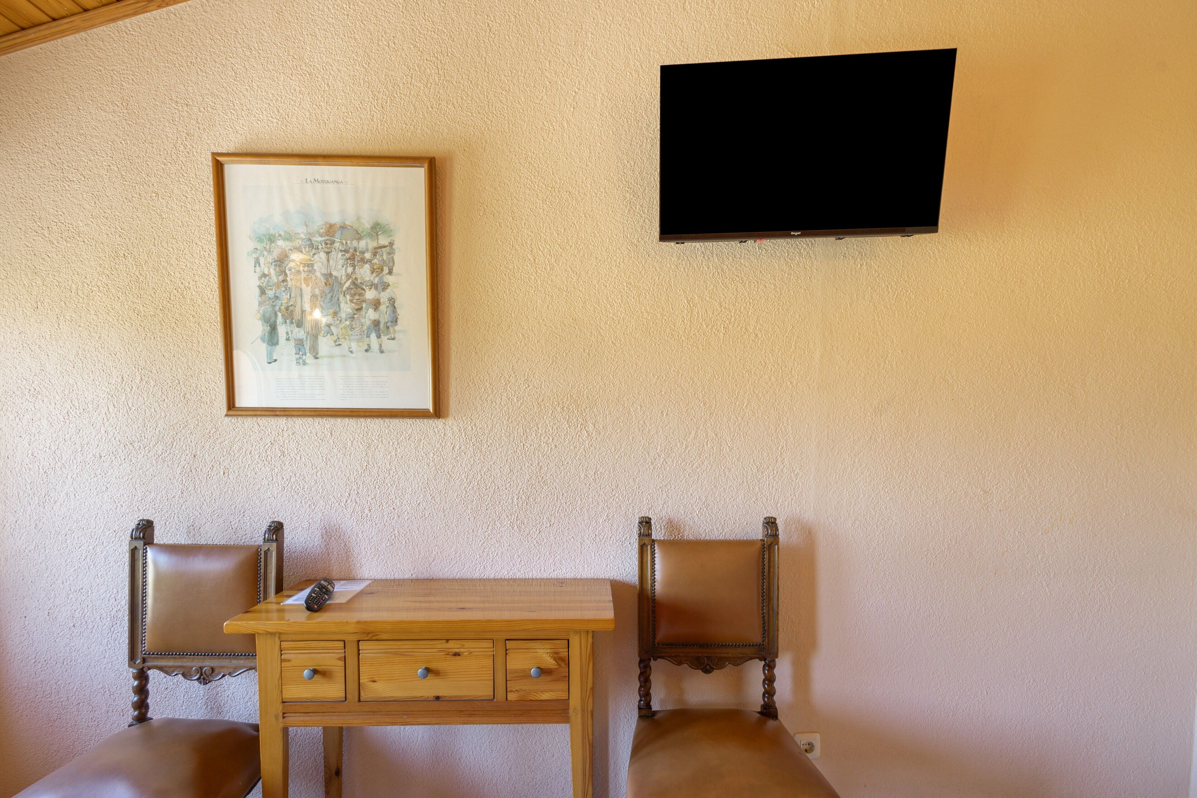 Ett rum med ett skrivbord i trä, två fåtöljer i läder, en inramad tavla och en väggmonterad tv.
