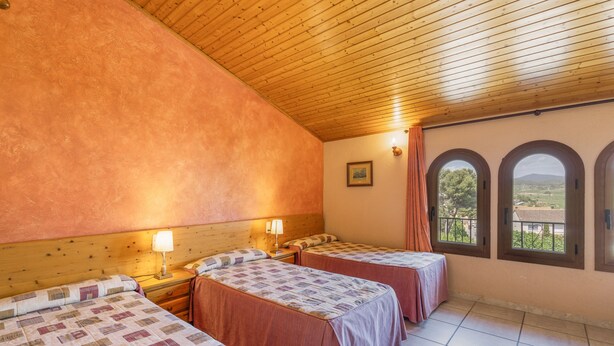Ein Zimmer mit zwei Betten, Holzboden, einem Fenster mit Blick und einem kleinen Tisch mit Lampe.