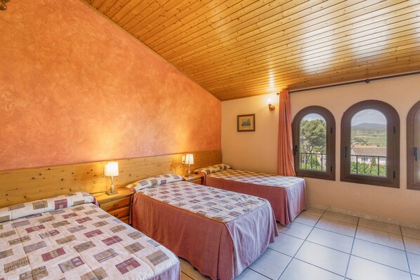 Una habitación con dos camas, techo de madera, ventana con vistas y una mesita con lámpara.