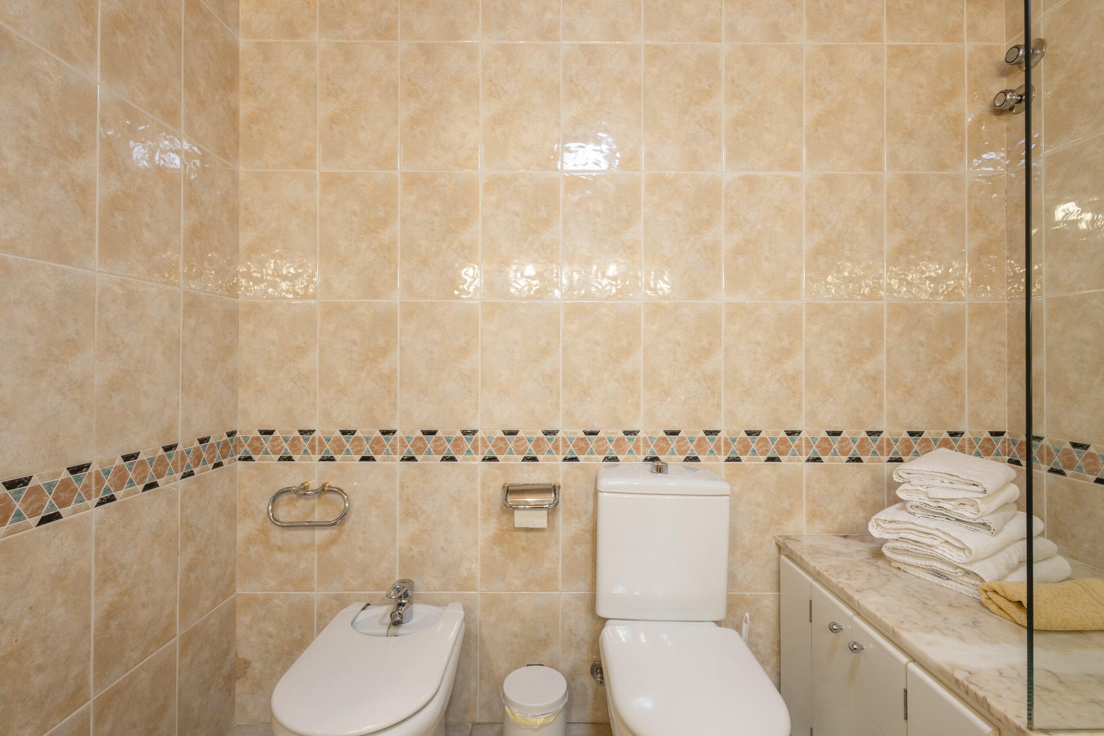 A bathroom with beige tiles, a toilet, a sink, a towel rack, and a mirror.