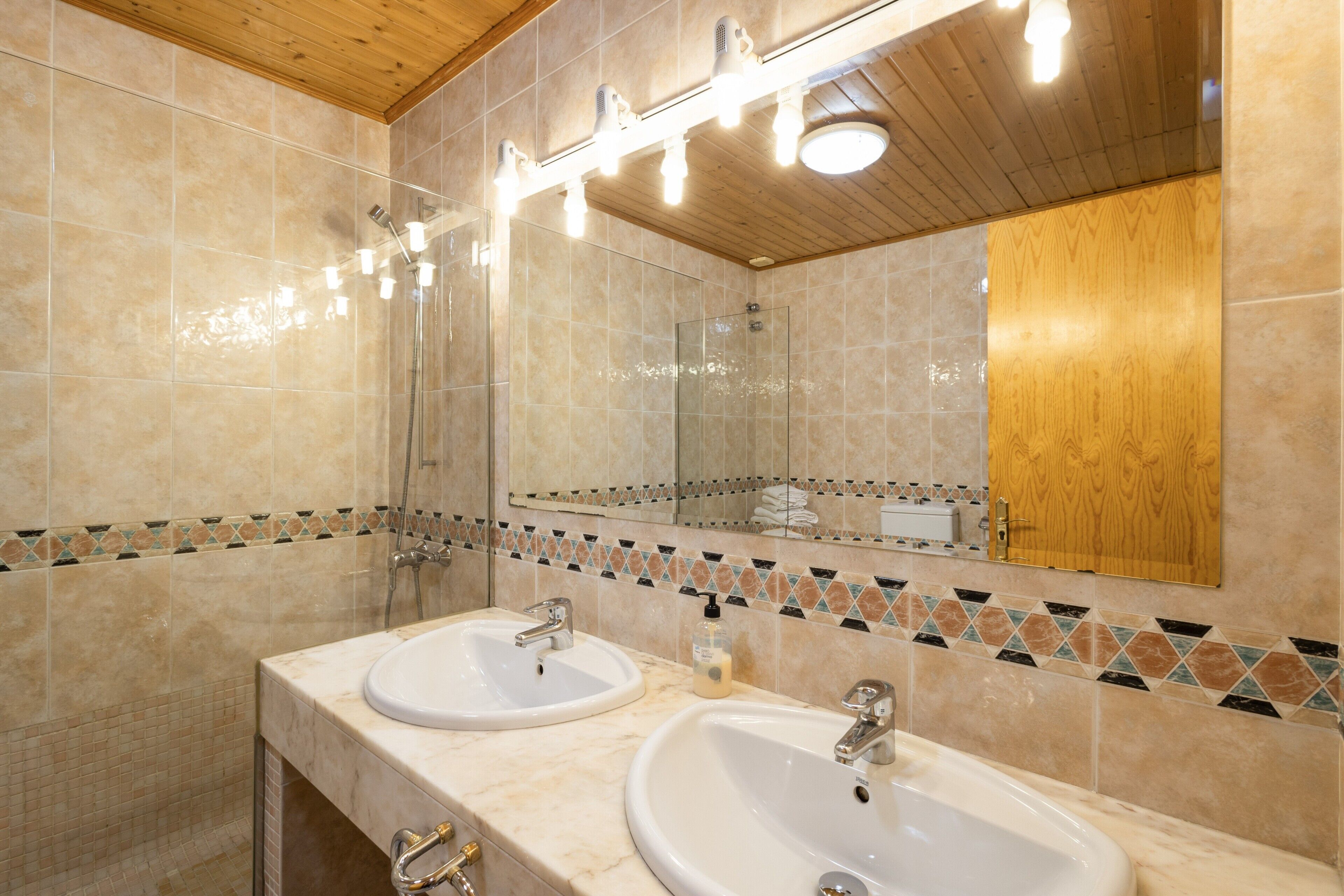 Un baño con dos lavamanos, una ducha y un espejo con iluminación.