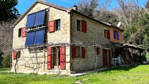 Una casa de piedra con contraventanas rojas, un panel solar y un jardín.