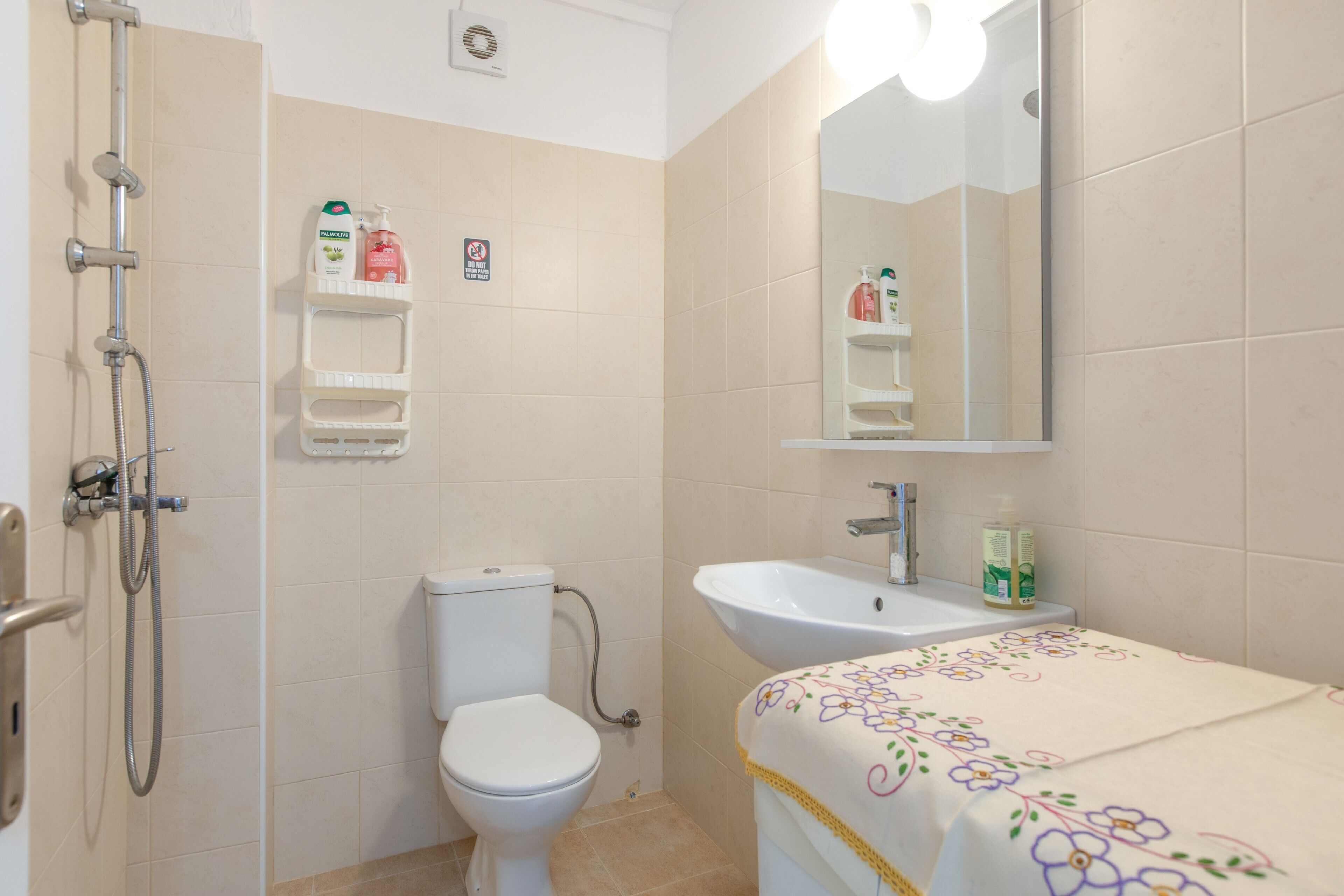 A bathroom with a toilet, shower, sink, and a mirror.